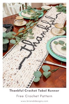 the table runner is decorated with green leaves and white plates, along with greenery