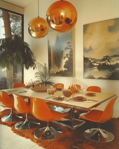 an orange dining room table surrounded by chairs and art on the wall in front of large windows