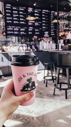 a person holding up a pink coffee cup in front of a restaurant with menus on the wall