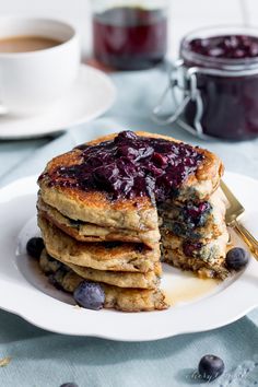 stack of pancakes with blueberries and syrup on plate next to cup of coffee or tea