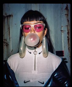 a woman wearing pink glasses blowing a bubble with her nose and nose ring on top of her head