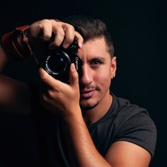 a man holding a camera up to his face in front of a black background,