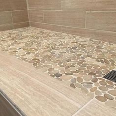 a bathroom with stone flooring and tile on the shower wall, along with a drain in the middle