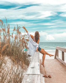 a woman is sitting on a wooden bench by the beach with her legs in the air