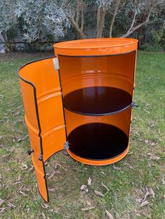 an orange metal trash can sitting in the grass