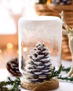 a glass jar filled with snow and pine cones sitting on top of a white table