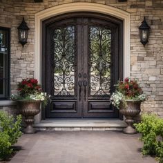 two large planters with flowers are in front of the entrance to a home that has stone walls and doors