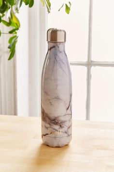 a marbled water bottle sitting on top of a wooden table next to a potted plant