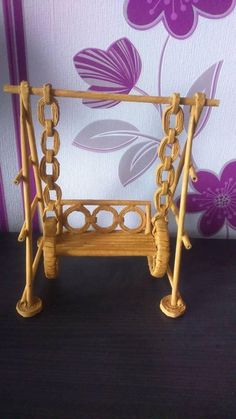 a miniature swing made out of wood on a black table with flowers in the background