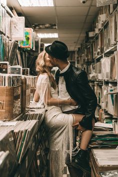 a man and woman are kissing in a record store, surrounded by stacks of records