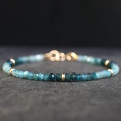 a blue beaded bracelet with gold beads on a gray surface and a black background