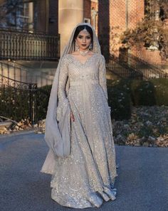 a woman in a silver gown and veil standing on the street with her hands behind her back