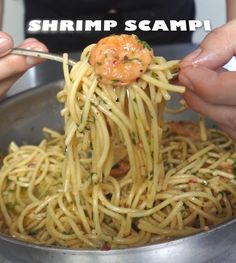 two hands holding a fork with shrimp scampi on it in a silver bowl