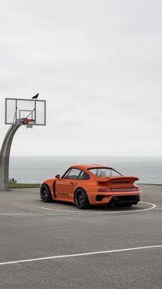 an orange sports car parked in front of a basketball hoop on top of a parking lot