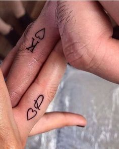 two people with tattoos on their fingers holding each other's hands and one has the word love written on it