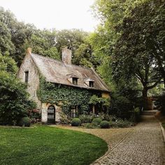 an old stone house with ivy growing on it's roof and brick walkway leading to the front door