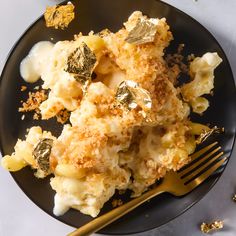 a black plate topped with macaroni and cheese covered in gold leafy toppings