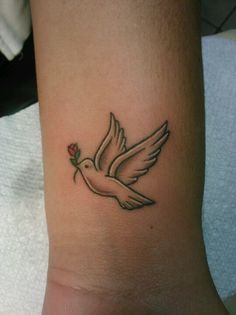 a small white bird with a red rose on its wrist tattooing it's wings