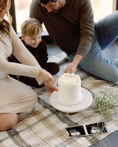 a man and woman cutting a cake with a small child sitting on the floor behind them