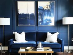 a living room with two blue couches and paintings on the wall