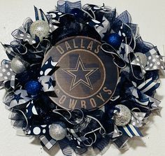 a black and white wreath with the word dallas cowboys painted on it, surrounded by silver and blue ornaments