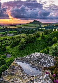 the sun is setting over some green hills and fields with flowers on them, as well as clouds in the sky