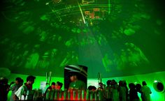 a group of people standing around in front of a projection on the wall and ceiling