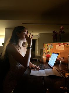 a woman sitting at a table drinking from a wine glass and using a laptop computer