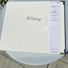 an open wedding album sitting on top of a white table next to a flower pot