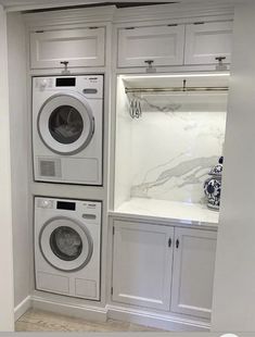 a washer and dryer in a white laundry room with built - in cabinets