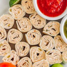 several wraps are arranged on a plate with dipping sauces and tomatoes in the background