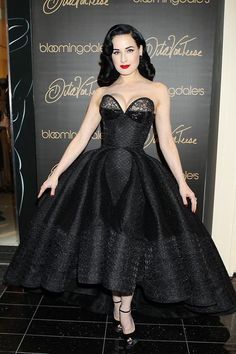 a woman in a black dress standing on a black tile floor next to a wall