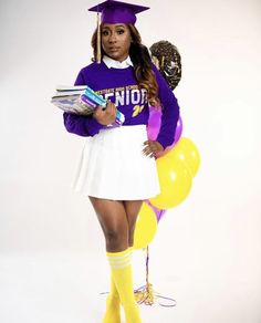 a woman in a purple and white graduation outfit is holding books while standing next to balloons