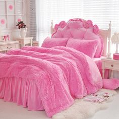 a bed with pink comforters and pillows in a white room next to a window