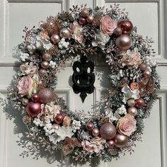 a wreath with flowers and ornaments hanging on the front door to decorate it for christmas