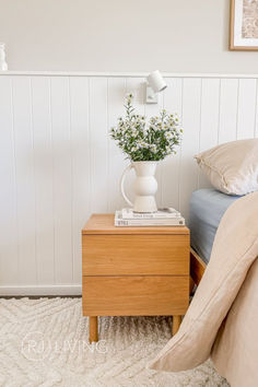 a bed room with a neatly made bed and a vase filled with flowers on the nightstand