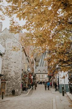 people are walking down the street in an old town with stone buildings and autumn leaves