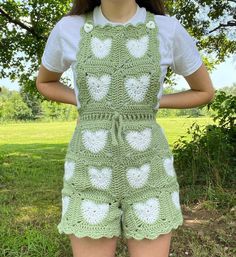 a woman wearing green crocheted overalls with white hearts on them