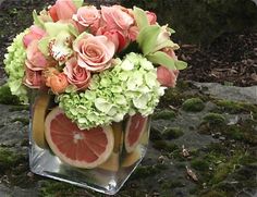 a vase filled with flowers and fruit on top of a moss covered rock ground in the woods