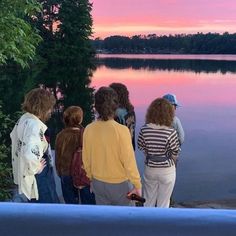 group of people standing on the edge of a body of water at sunset with trees in the background