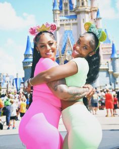 two women hugging each other in front of a castle at disney world with people around them