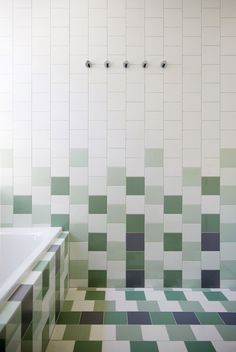 a bathroom with green and white tiles on the wall, tub and shower head in the corner