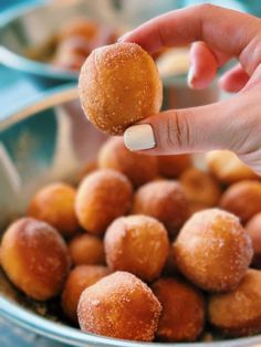 a hand picking up a donut from a bowl filled with sugared donuts