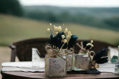 three jars with flowers are sitting on a wooden table in the middle of a field