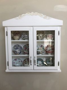 a white china cabinet with glass doors and plates on it