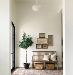 a living room with white walls and pictures on the wall, a wooden bench next to a potted plant