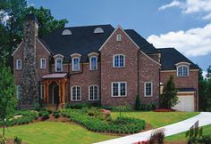 a large brick house with lots of windows and landscaping around the front door, along side a driveway