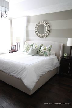 a bed with white sheets and pillows in a bedroom next to a large mirror on the wall