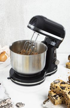 an electric mixer with cookies and chocolate chip cookie bars next to it on a white surface