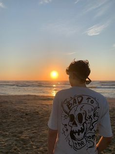 a man standing on top of a sandy beach next to the ocean at sun set